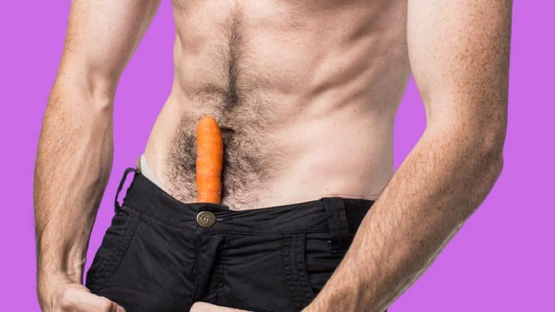 A photo of a man displaying penile girth enlargement techniques with a carrot in his pants.