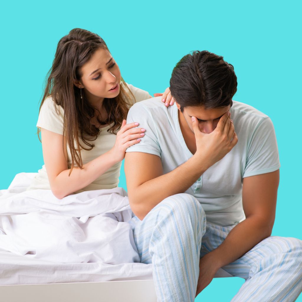 An image showing a frustrated man with Erectile Dysfunction sitting on a bed with his wife